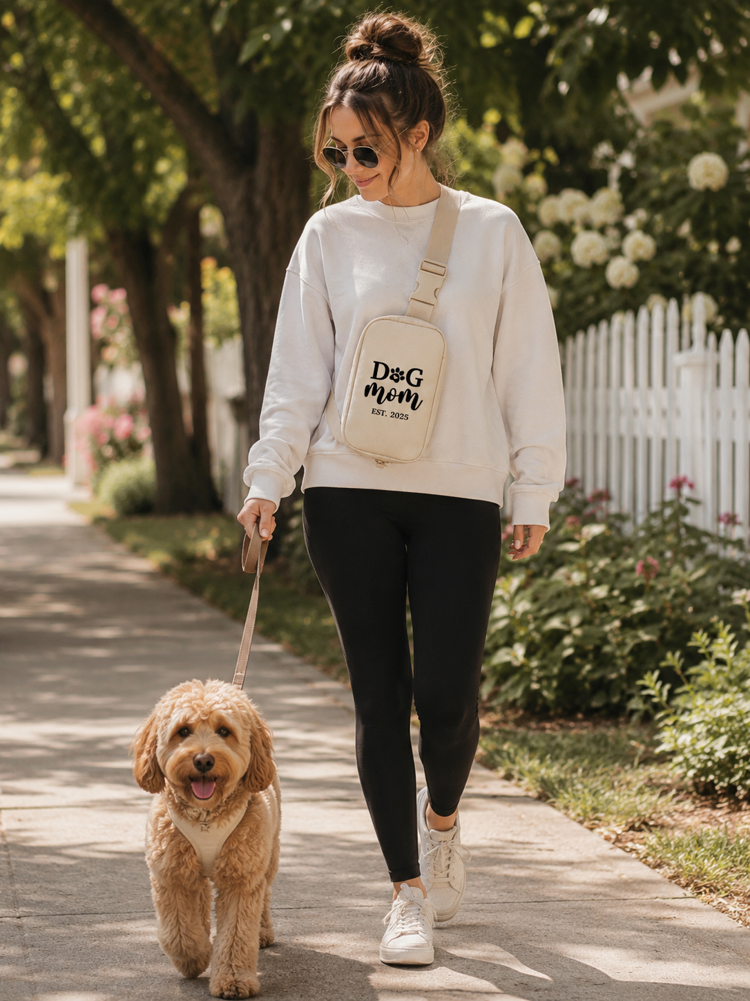 Woman walking a dog on a leash with a 'Dog Mom' bag in a park-like setting.