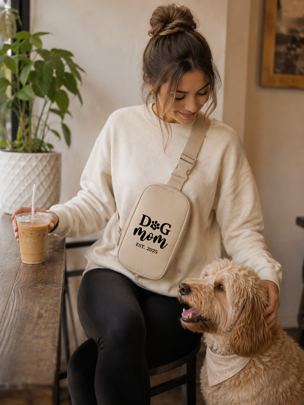 Woman with a 'Dog Mom' bag sitting at a table with a dog, holding a drink.