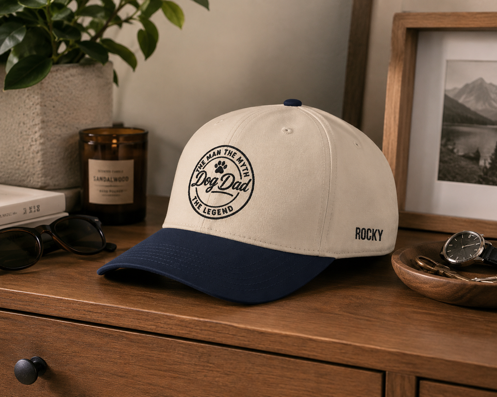 Beige and navy cap with 'Dog Dad' text on a wooden surface with decor items.