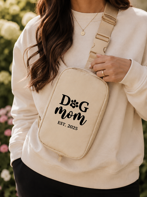 Person wearing a beige crossbody bag with 'Dog Mom EST. 2025' text, outdoors.