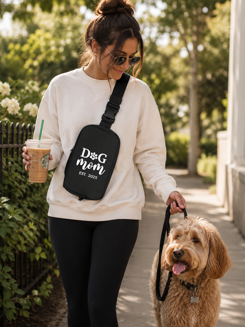 Woman walking a dog while holding a Starbucks cup, wearing a custom 'Dog Mom' bag.